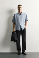 Camisa regular fit confeccionada en tejido de lino, color blanco, con cuello solapa, manga corta y cierre frontal de botonadura.