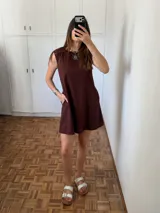 Vestido corto sin mangas, de corte amplio y recto, color marrón oscuro (chocolate). Confeccionado en lino de algodón, presenta bolsillos laterales y un tajo en la espalda con lazo regulable.