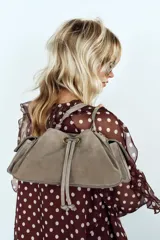 Mini bolso bandolera de piel color gris topo, con diseño fruncido, cierre mediante cordón ajustable y stopper, bolsillos exteriores laterales con solapa y botón imantado, y correa ajustable.