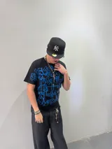 Remera negra de corte regular con estampado frontal de gran tamaño en serigrafía color azul, con diseño de caligrafía abstracta. Cuenta con cuello reforzado y grifa de la marca en la manga.