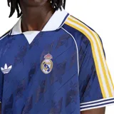 Camiseta de fútbol Adidas Originals del Real Madrid, color azul oscuro con estampado jacquard de logotipos. Presenta cuello polo blanco, mangas con las icónicas tres tiras en amarillo y detalles en blanco y azul en los puños.
