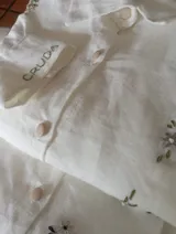 Camisa de lino color crudo con bordados artesanales florales y cierre frontal con botones forrados. Presenta detalle bordado en el puño.