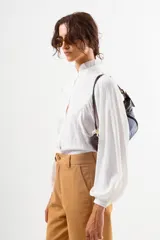 Camisa blanca de manga larga con cuello alto fruncido y puños ajustados. Presenta un corte holgado y tela con textura ligera.