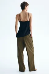 Pantalón verde militar de corte holgado, con pinzas delanteras, bolsillos laterales, bolsillos traseros decorativos y piernas amplias con pliegues marcados. Cuenta con cierre de botón y corchetes ocultos.