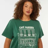 Remera de algodón color verde oscuro, corte holgado y manga corta, con estampado frontal en blanco que simula la fachada de un café parisino con el texto "CAFÉ PARISIEN".