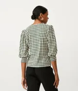 Blusa de jersey con estampado geométrico en tonos blanco, negro y verde. Tiene escote en V, mangas 3/4 abullonadas con elástico en los puños y cierre frontal con botones.
