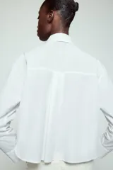Camisa blanca de cuello solapa y manga larga, con detalle de lazada en el mismo tejido en la parte frontal y cierre con botones dorados.