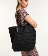 Bolso de playa tejido en paja de papel color negro, con asas de cuero sintético y cierre a presión. Incluye borla decorativa colgante.