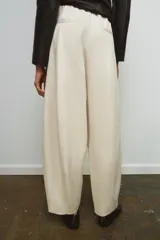 Pantalón de tiro medio color beige claro, de pierna ancha y corte balloon. Presenta pliegues frontales y bolsillos delanteros ocultos en costura.