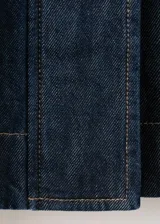 Parka oversize de tejido denim color azul oscuro, con cuello alto, mangas raglán largas, bolsillos laterales, cintura elástica y cierre frontal con botones ocultos.