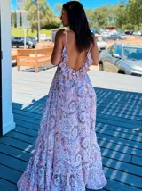 Vestido largo tipo solera, con escote en V profundo y tirantes finos. Presenta un estampado paisley en tonos rosados, lilas y blancos, con ajuste de lazo en la cintura y volados en el ruedo.