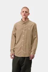Camisa de manga larga Carhartt WIP modelo L/S Madison Fine Cord, color beige de pana fina de algodón. Cuenta con cuello abotonado, cierre frontal de botones, dobladillo curvo y el logo bordado de la marca en el pecho.
