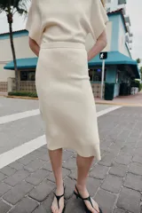 Falda midi de punto color crudo, con tiro medio, cintura elástica y diseño evasé.