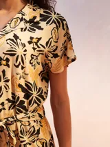 Mono corto negro con estampado floral en tonos beige y amarillo. Presenta cuello camisero, manga corta y un lazo ajustable en la cintura.
