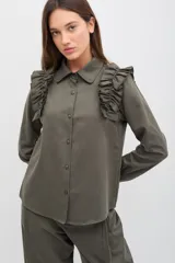 Camisa de gabardina de tencel color negro, con cuello clásico, cierre frontal de botones y volados fruncidos en los hombros.