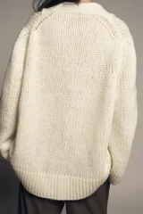 Chaqueta de punto de lana con cuello en pico, manga larga y cierre frontal con botones oscuros. Presenta un diseño de tejido grueso y holgado.