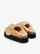 Zueco negro de cuero con plataforma y plantilla recubierta de piel de oveja. Presenta una hebilla dorada de gran tamaño en la capellada.