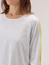 Remera de manga larga color gris claro, con detalle de franjas laterales en contraste color amarillo en las mangas. Presenta un diseño holgado y moderno.
