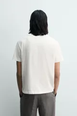 Camiseta de manga corta y cuello redondo, color blanco roto con efecto lavado y desgastado. Presenta un estampado frontal en negro con texto de estilo universitario que incluye "PRINCE ST.", "GROOVE ALLEY", "SOHO, NYC" y el número "95".