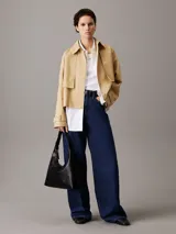 Cartera tipo hobo de piel sintética negra, con silueta fluida y correa ajustable con herrajes metálicos. Presenta cierre de cremallera principal y logo Calvin Klein grabado en la parte delantera.