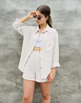 Conjunto de camisa y short a rayas verticales color beige y blanco. La camisa es de manga larga con botones dorados y un bolsillo en el pecho. El short es de tiro alto con elástico en la cintura.