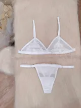 Conjunto de lencería compuesto por un corpiño triangular de microtul transparente con detalles de encaje floral y una tanga regulable a juego.