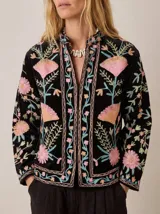 Chaqueta de terciopelo negro con cuello mao, corte recto y cierre frontal central, decorada con un elaborado bordado floral en tonos rosados, dorados y celestes de inspiración suzani.