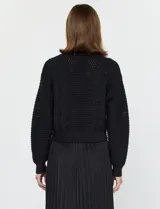 Conjunto compuesto por un buzo de tejido calado con cuello redondo y mangas largas, y un vestido midi de satén con falda plisada. Ambas piezas son de color negro y pueden combinarse o utilizarse por separado.