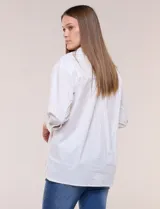 Camisa de silueta holgada y largo extendido, confeccionada en poplín elástico de color blanco. Presenta cuello solapa abierto en V con cartera frontal de abotonadura oculta, hombros caídos y mangas tres cuartos. Cuenta con espalda con canesú, pliegue central y ruedo recto con pequeñas aberturas laterales.