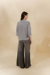 Pantalón de jean gris oscuro, estilo sastrero de tiro medio bajo y corte ancho (wide leg). Presenta costuras marcadas en el frente y un cinturón trenzado marrón con hebilla metálica.