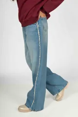 Pantalón de jean celeste de corte wide leg con detalle de flecos blancos en los laterales.