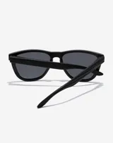 Lentes de sol unisex Hawkers modelo One Raw Carbono, con montura cuadrada negra con textura de fibra de carbono y lentes polarizadas oscuras.