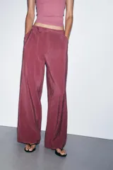 Pantalón de tiro alto color bordó, de corte ancho y pierna recta, con pinzas frontales y lazada ajustable en la cintura. El tejido presenta un acabado satinado o ligeramente arrugado.