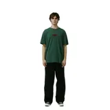 Remera de algodón color verde oscuro con efecto lavado, corte holgado y un pequeño logo ovalado bordado en rojo en el pecho.