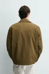 Parka de corte relajado confeccionada en mezcla de algodón color marrón. Presenta cuello solapa, cierre frontal con cremallera oculta y alamares metálicos, bolsillos de plastrón con solapa en la cadera y bolsillo de vivo en el pecho.