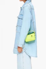 Bolso bandolera tipo hobo de piel color amarillo flúor, tamaño mini, con cierre de cremallera, asa de mano con apliques de caritas sonrientes y asa bandolera metálica extraíble.