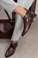 Bota corta color borgoña con textura de reptil, puntera fina, elástico negro en el empeine y talón descubierto.