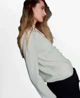 Blusa de manga larga en color crema, con cuello alto y diseño de drapeado suave en la parte frontal. Presenta un corte recto y elegante.