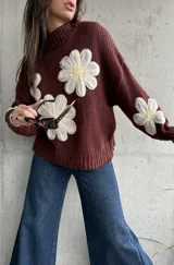 Sweater de punto color chocolate con diseño de flores grandes en relieve en color crema y centro amarillo. Presenta cuello alto, mangas largas y corte holgado.