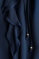 Blusa de crepé de gasa color azul marino, con cuello mao y abertura frontal con tiras finas. Presenta un diseño holgado con volados verticales en el frente, mangas largas tipo globo con corte raglán y puños elásticos con volados.