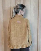 Sobrecamisa de pana color marrón oscuro, con cuello camisero, cierre frontal de botones y detalle de volado en el ruedo. Presenta mangas largas con puños y bolsillos frontales aplicados.