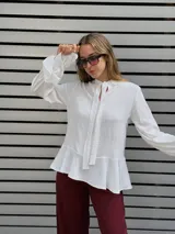 Blusa blanca de textura arrugada, con escote en V y lazos para anudar. Presenta mangas largas con puños acampanados y un diseño con volado en el ruedo.