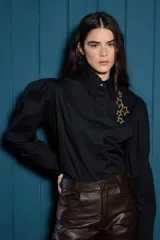 Camisa de corte clásico color blanco, con mangas largas abullonadas en los hombros y puños abotonados. Presenta un detalle de estrellas bordadas en color dorado sobre el lado izquierdo del pecho.