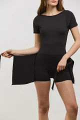 Vestido deportivo corto de color negro, diseñado para pádel. Presenta una estructura superior tipo remera de manga corta con espalda abierta, y una parte inferior que combina una calza corta con una media pollera envolvente que se ata en la cintura. Confeccionado en tejido suave y elástico.