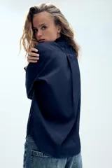Camisa oversize de nylon color azul marino, con cuello solapa, manga larga, bolsillo de parche en el pecho y cierre frontal con cremallera.