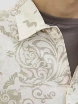 Camisa de manga corta con cuello resort, confeccionada en una mezcla de algodón y lino. Presenta un diseño estampado con motivos tipo damasco en tonos neutros y un corte amplio.