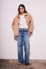 Sobrecamisa negra de estilo shacket, confeccionada en tejido de gamuza sintética. Presenta cuello camisero, cierre frontal de botones y dos bolsillos de parche con solapa en el pecho. El calce es oversize y las mangas son largas.