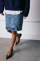Falda midi de tiro medio confeccionada en denim con efecto lavado. Presenta cintura con trabillas, cierre frontal con cremallera, botón y gancho metálico, y una abertura en el bajo.