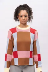 Buzo de punto con diseño geométrico de cuadros en tonos marrón, celeste, rosa y rojo. Presenta cuello redondo, puños y ruedo en color crema, con mangas largas y corte recto.