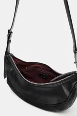 Bolso de hombro con diseño de media luna, confeccionado en material sintético con acabado texturizado. Cuenta con cierre de cremallera superior, asa ajustable con hebilla y detalle de mosquetón metálico en uno de los extremos.